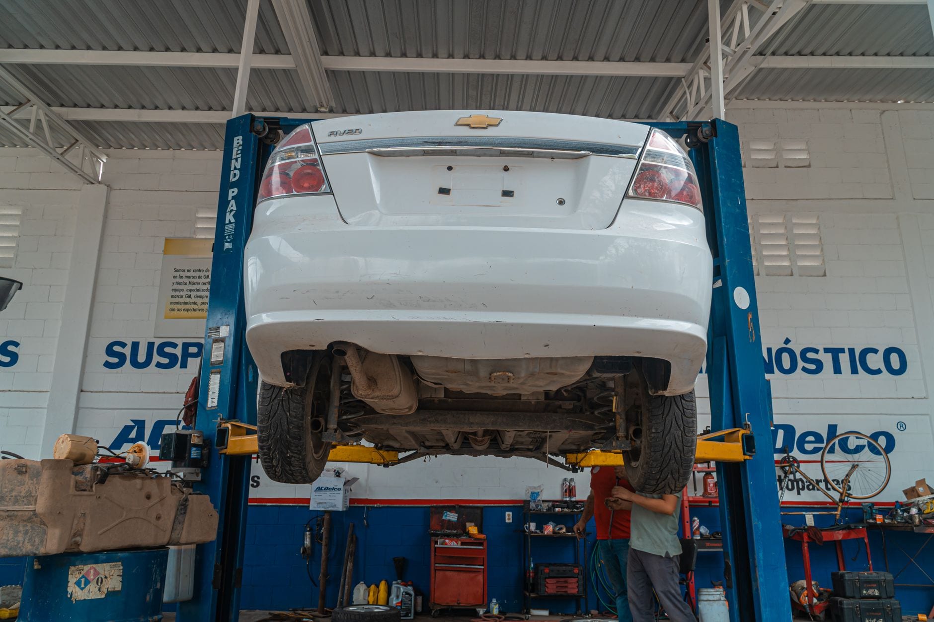 A white Chevrolet car is lifted for maintenance in an automotive repair shop.